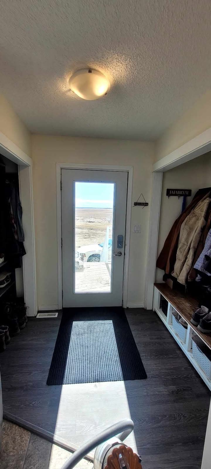 Entryway with a glass door, black mat, and coats hanging on a built-in bench.