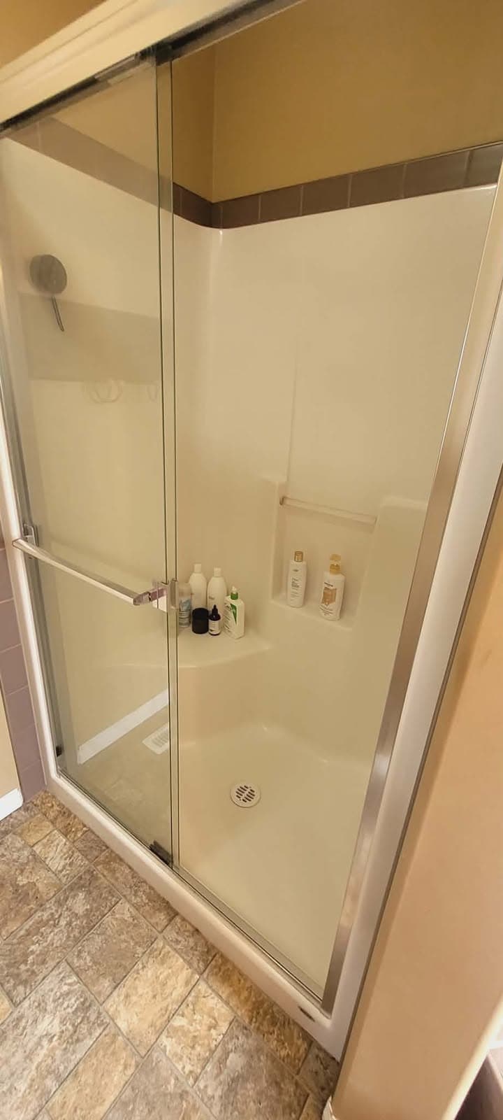 Walk-in shower with sliding glass doors, white interior, built-in shelves, and various toiletry bottles.
